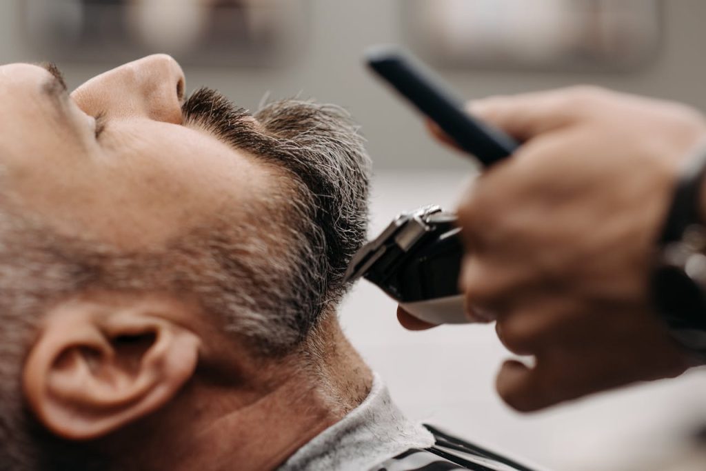 Close-up of a barber using clippers to groom a clients beard in a barbershop.