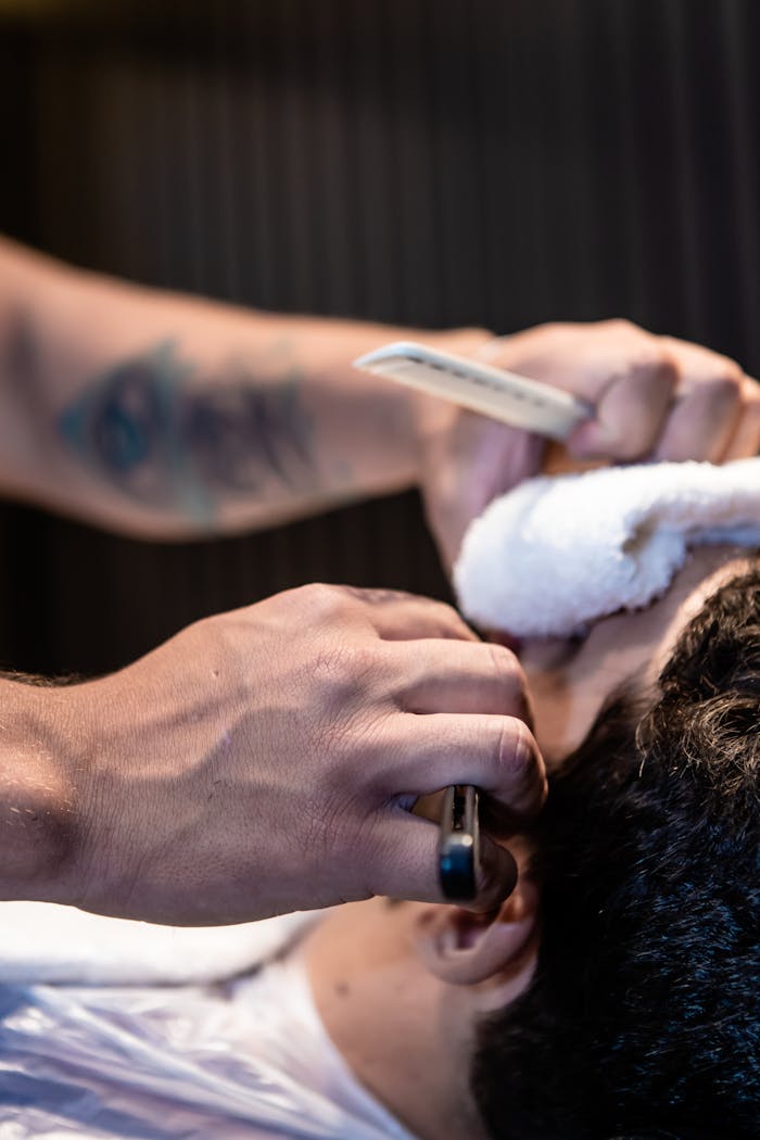 A barber uses a razor to shave a customer inside a barbershop.