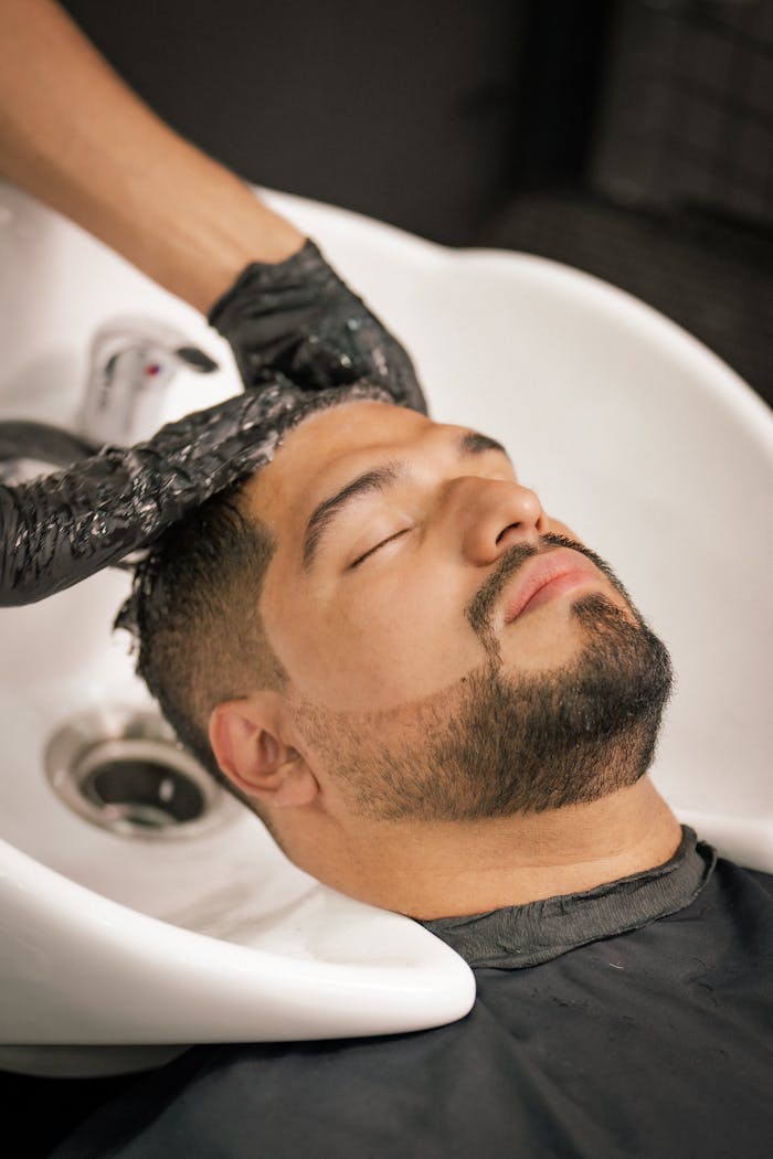 A man with closed eyes enjoys a calming hair wash at a barbershop sink.