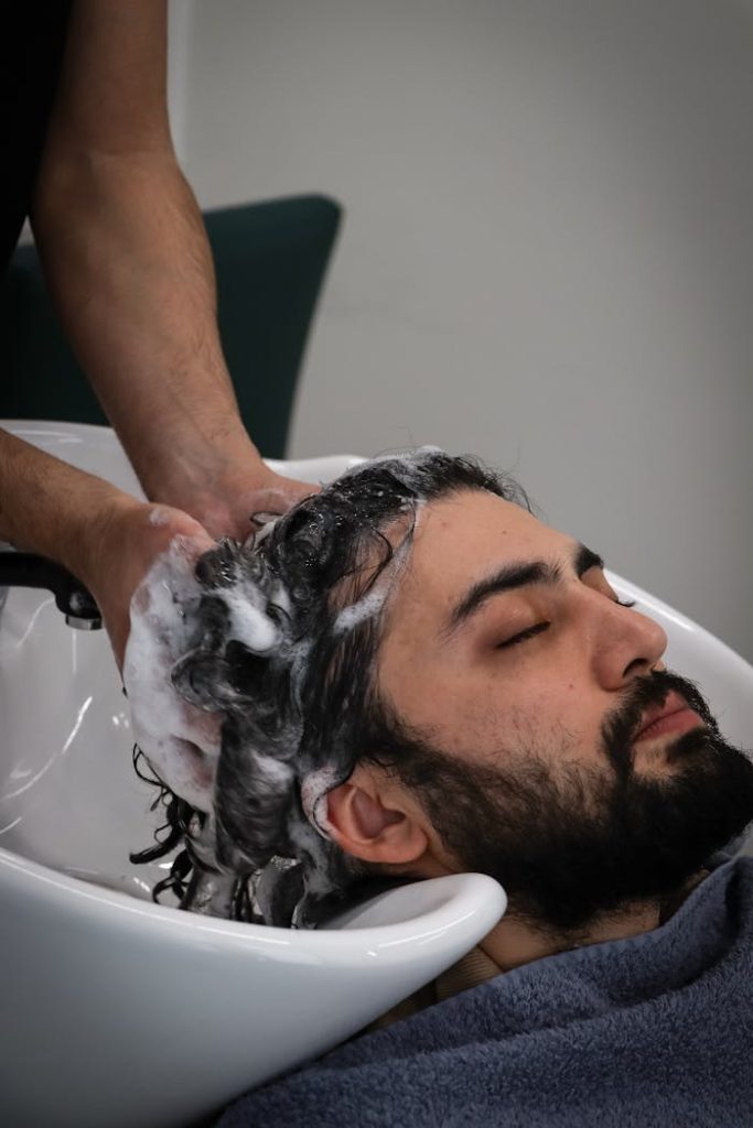 Relaxed man with beard getting hair washed at salon sink. Spa and grooming concept.