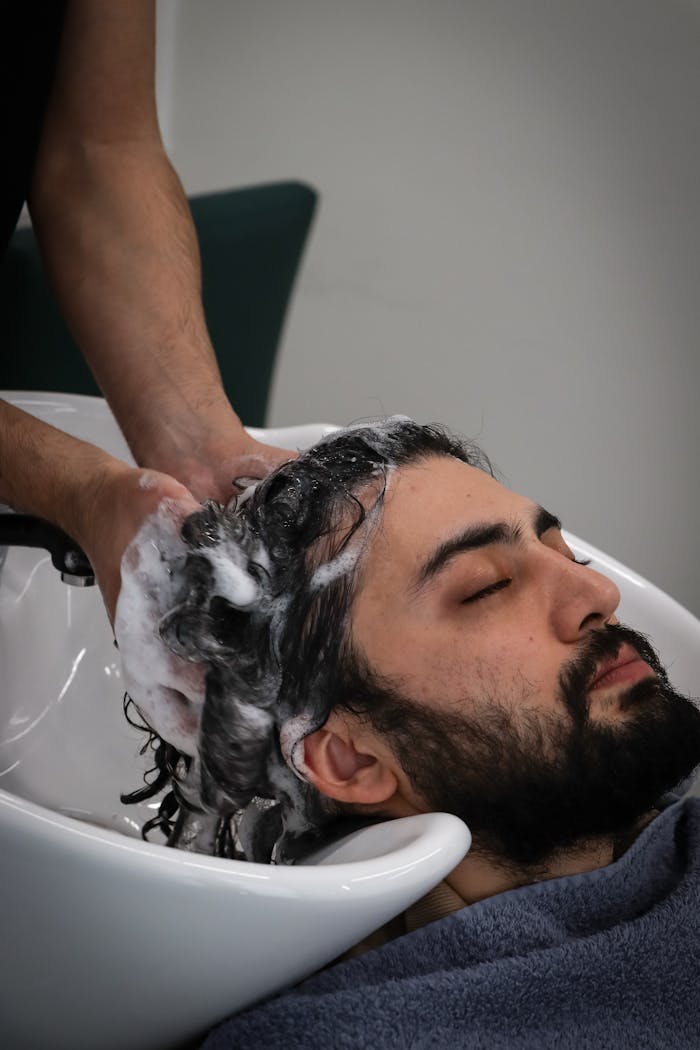 Relaxed man with beard getting hair washed at salon sink. Spa and grooming concept.